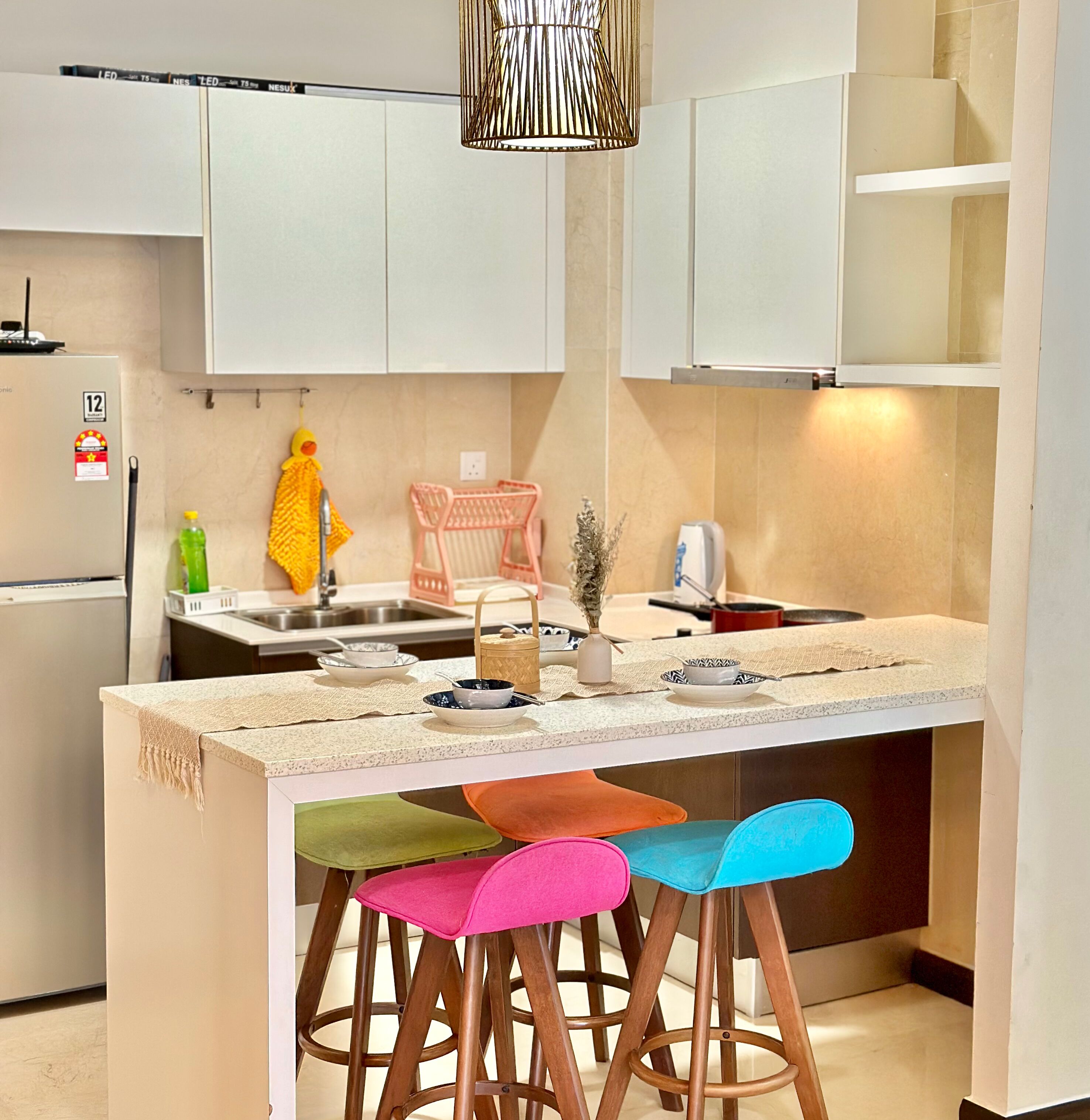 A modern kitchen with white cabinets, a stainless steel sink, and a bar area with colorful stools.
