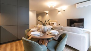 A modern dining area with a round table set for four, surrounded by green upholstered chairs. A sofa and a flat-screen TV are visible in the background. - RUAH D - Delightful Studio by LovelyStay (Vila Nova de Gaia)