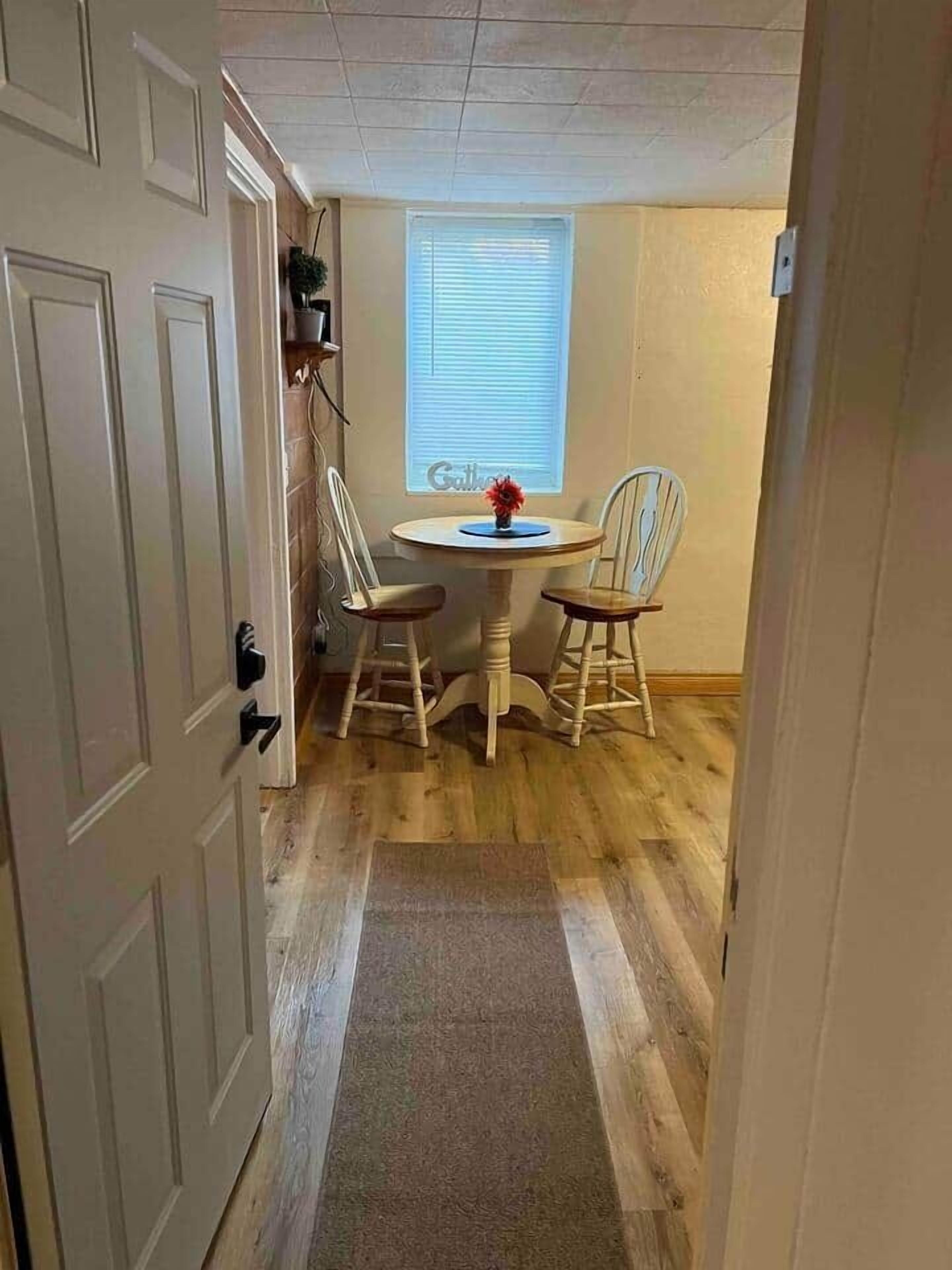 A room with a dining table, two chairs, a window with blinds, and a door.