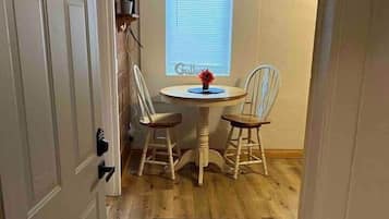 A room with a dining table, two chairs, a window with blinds, and a door.