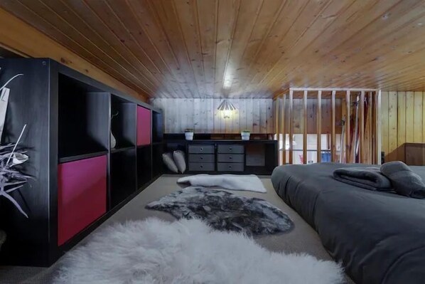 Une pièce comprenant un lit, une armoire noire et rose, un petit coin cuisine et un plafond en bois.