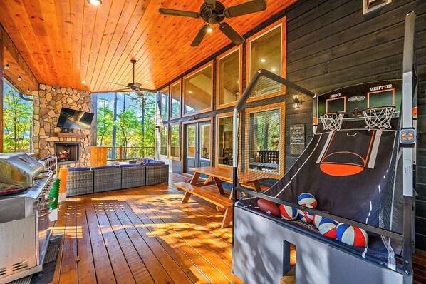 Una terraza de madera con una parrilla, chimenea de piedra y una cancha de baloncesto.