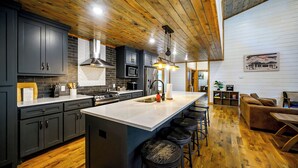 A modern kitchen with dark cabinets, a large island, and a wooden ceiling. - 2 Kings + Bunk Haus | Fun Games | Hot Tub | Wheelchair Access, Sleeps 11, Pets (Broken Bow)