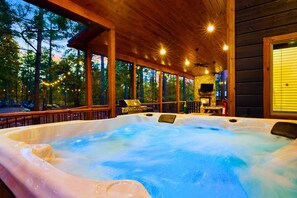 Un jacuzzi en una cabaña de madera con pared de piedra, una parrilla y un televisor.