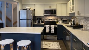 A modern kitchen with stainless steel appliances, white cabinets, and a central island with bar stools. - Newly renovated Townhouse walking distance to Mt.Snow base lodge.  (Dover)