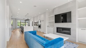 A modern kitchen with white cabinetry, a built-in oven, and a large TV mounted on the wall. - Modern family-sized house close to 17th Ave and downtown (Calgary)