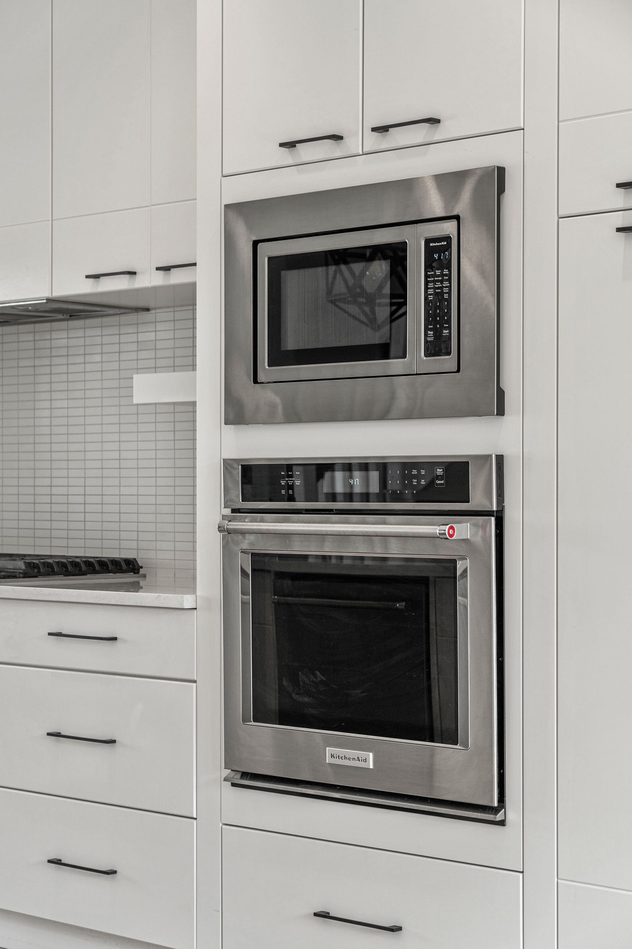 Una cocina con microondas y horno integrados, muebles de cocina blancos y salpicadero de azulejos.