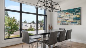 A modern dining area with a large window, a contemporary chandelier, and a piece of abstract art on the wall. - Modern family-sized house close to 17th Ave and downtown (Calgary)