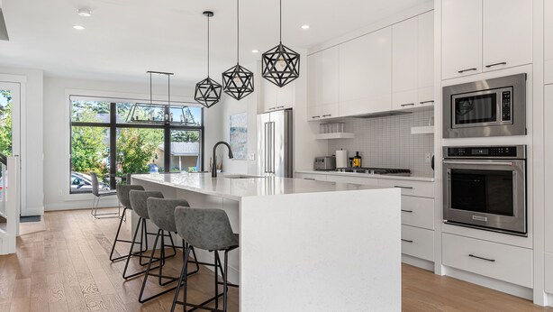 A modern kitchen with a large island, stainless steel appliances, and bar stools. - Modern family-sized house close to 17th Ave and downtown (Calgary)