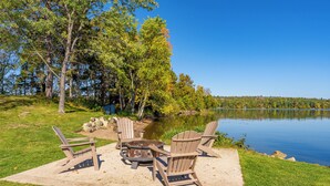 Ein Sitzbereich im Freien mit Adirondack-Stühlen und einem Feuerkorb am See.