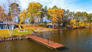 Eine Holzstege ragt in einen See hinein, umgeben von Bäumen mit Herbstlaub.