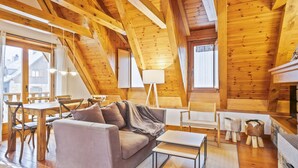 Ein gemütlicher Loftsraum mit Holzbalkendecke, einer Couch, einem Esstisch und einem Kamin.
