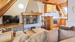 Ein gemütlicher Wohnraum im Loft-Stil mit Kamin aus Stein, Holzbalken, Fernseher und einer Küchenzeile.