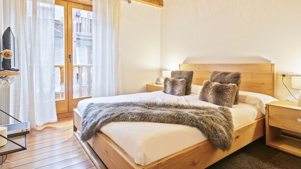 Ein hölzernes Bett mit einer flauschigen Decke, einem Holzkopfstück und zwei Nachttischen mit Lampen.
