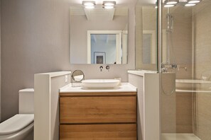 A modern bathroom with a wooden vanity, a large mirror, and a glass shower enclosure.