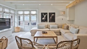 Ein geräumiges Wohnzimmer mit einer großen Couch, einem Couchtisch und Korbstühlen. An den Wänden befinden sich zwei Bilder von Wildtieren.