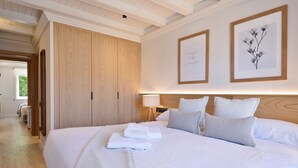 Una cama grande con sábanas blancas, un armario de madera y dos cuadros en la pared.