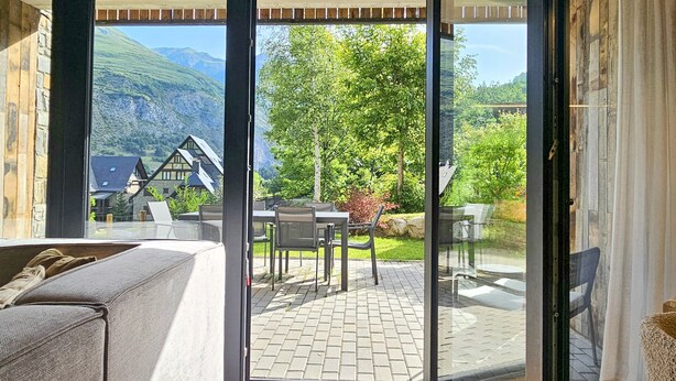 A modern room with a sliding glass door leading to an outdoor patio. The patio has a brick floor and is furnished with a table and chairs. - Luderna - Apartamento con jardín Marconi (Arties)