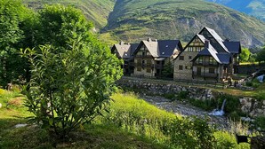 A traditional stone building with multiple rooms, situated by a stream with a waterfall, surrounded by lush green hills. - Luderna - Apartamento con jardín Marconi (Arties)