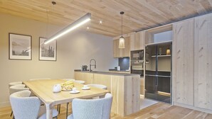 A modern kitchen with wooden cabinetry, a central island, and a dining area with four chairs. - Luderna - Apartamento con jardín Marconi (Arties)