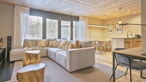 A modern living room with a sectional sofa, wooden flooring, and large windows. - Luderna - Apartamento con jardín Marconi (Arties)