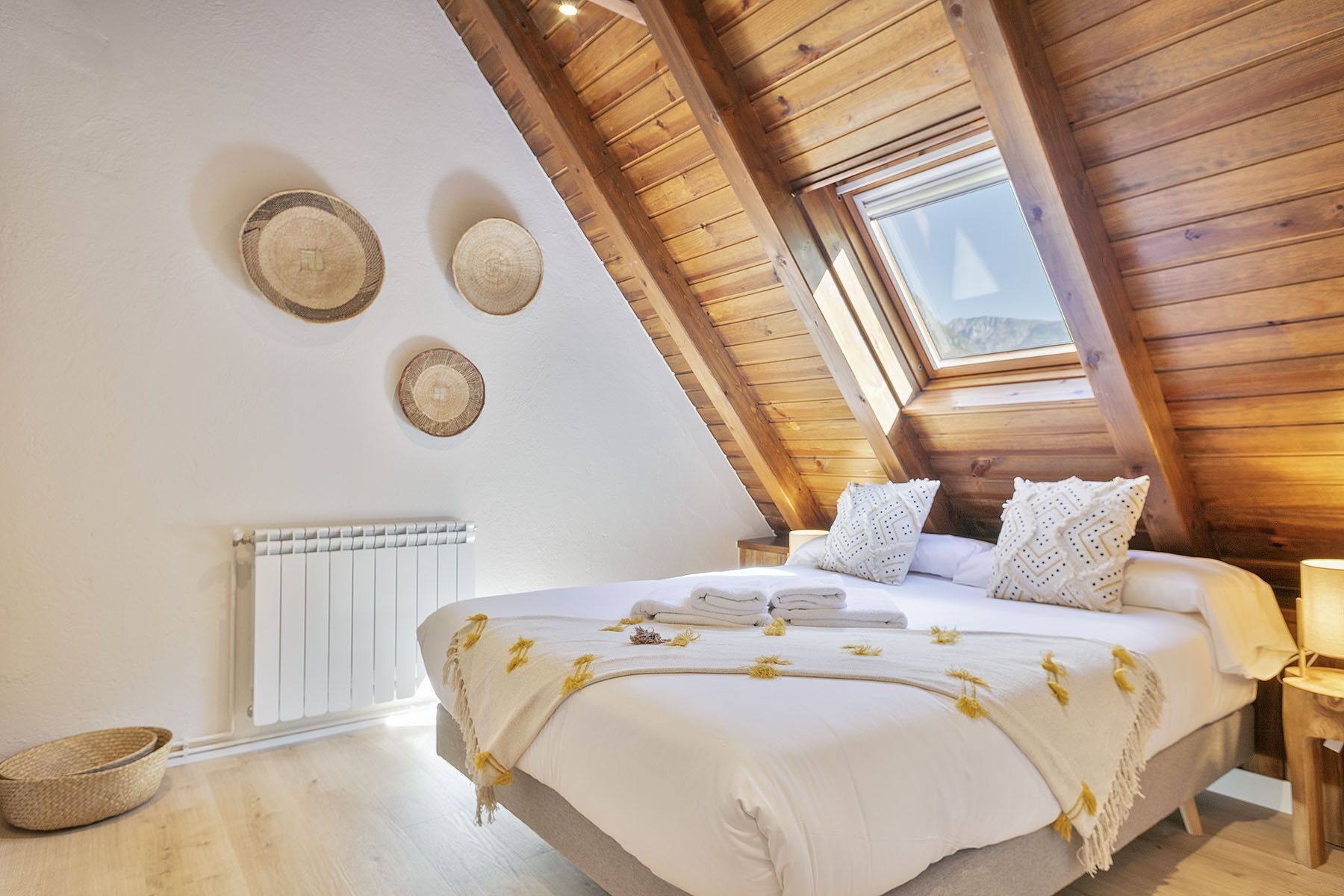 Un dormitorio con techo inclinado, una cama con ropa de cama blanca, un ventanal y tres adornos circulares colgados en la pared.