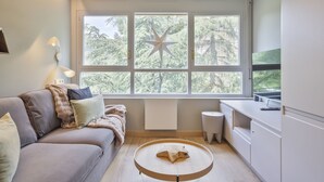Een moderne woonkamer met een bank, een ronde houten tafel, een sterrenstelsel decoratie op het raam en uitzicht op bomen.