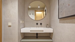Een badkamer met een ronde spiegel, een witte wastafel en beige tegels.