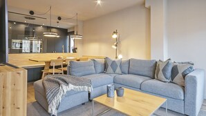A modern living room with a grey sofa, a wooden coffee table, and a kitchen area in the background. - Luderna - Apartamento con terraza Montanero (Vielha)