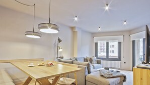 A modern living room with a wooden dining table, a sofa, and a television. - Luderna - Apartamento con terraza Montanero (Vielha)