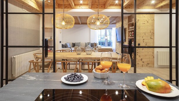 Uma área de refeições com uma mesa posta para o café da manhã, incluindo um prato de amoras, uma tigela de croissants e um copo de suco de laranja.