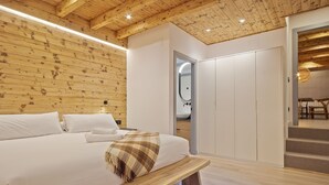 Quarto com teto de madeira, cama com roupa de cama branca, um banco e um guarda-roupa.