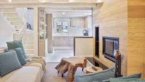 Um interior moderno com uma escada que leva a uma cozinha, uma área de estar aconchegante com uma mesa de centro de madeira e uma televisão de tela plana fixada na parede.