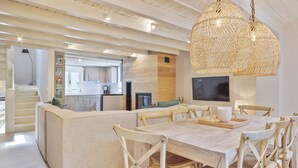 Uma sala de estar ampla com uma grande mesa de jantar, assentos confortáveis e uma cozinha ao fundo.