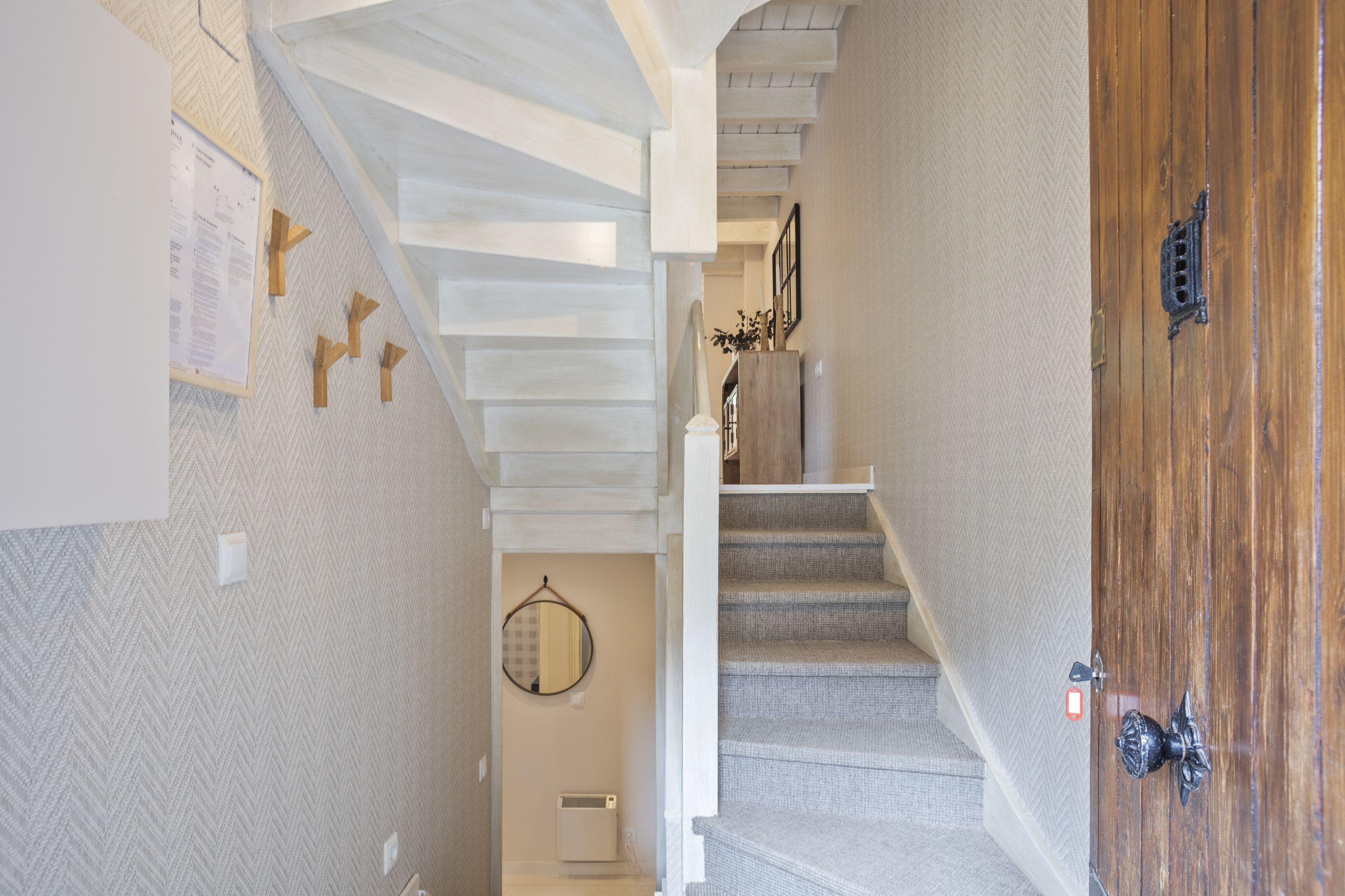 Un escalier avec une porte en bois, un mur orné d’un motif en chevrons et un miroir.