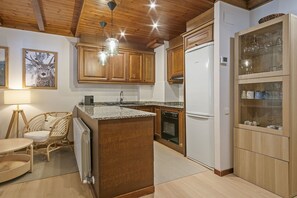 A kitchen with wooden cabinets, a built-in island, a refrigerator, and a glass-fronted cabinet with dishes. - Luderna - Val de Ruda B135 Era Tringòla (Baqueira)