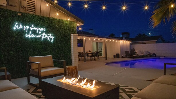 An outdoor patio with a fire feature, lounge chairs, and a neon sign.