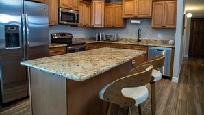 A modern kitchen with wooden cabinets, stainless steel appliances, granite countertops, and a central island with bar stools.