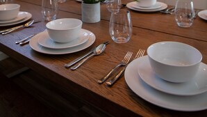 A dining table set with white plates, bowls, and cutlery, a potted plant, and a modern chandelier.