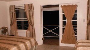 A bedroom with two beds, a window with curtains, and a door leading to an outdoor area. - Bahamas Fishing Lodge Hotel
Acklins Island (Salina Point)