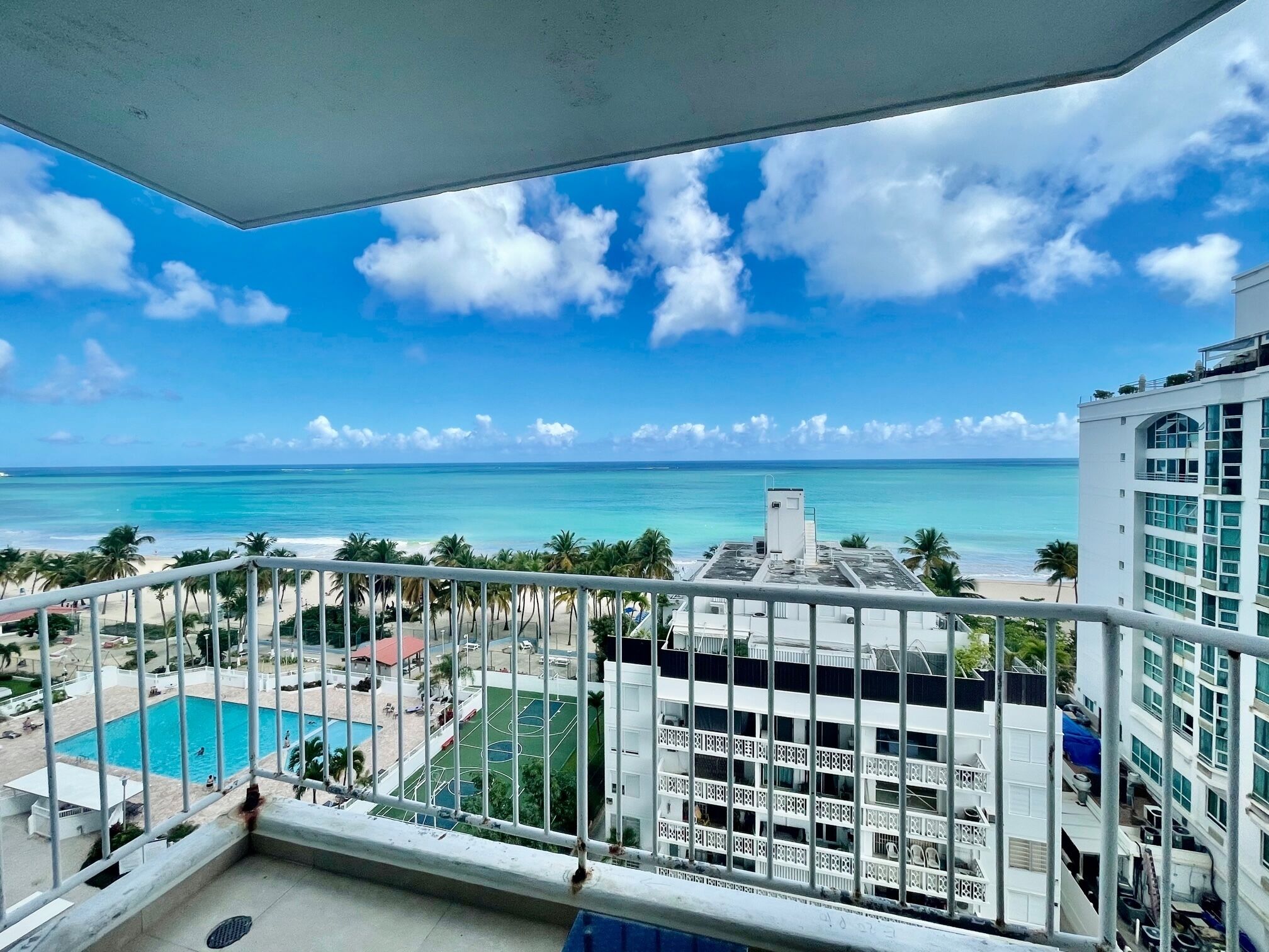 Ein Balkon mit Blick auf einen Strand, ein Schwimmbad und ein mehrstöckiges Gebäude.