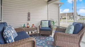 A covered patio area with wicker furniture, a patterned rug, and a view of a residential neighborhood.