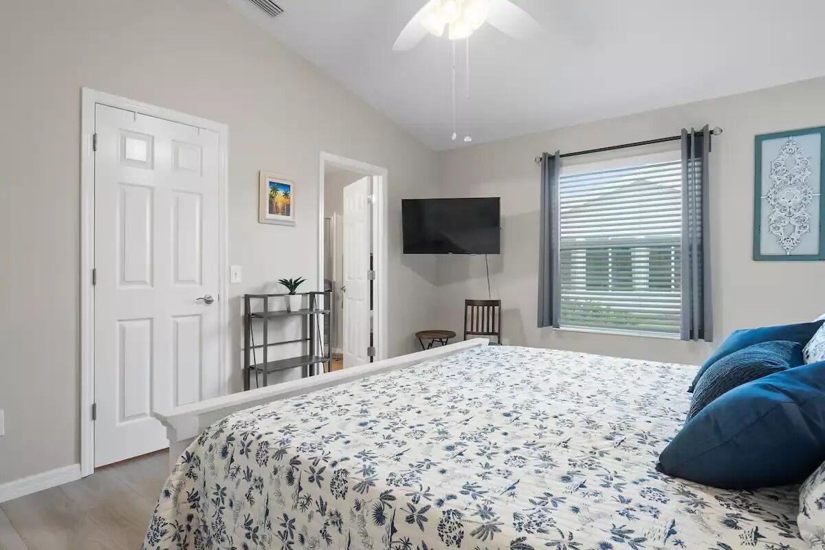 A bedroom with a bed, a TV, a window with blinds, and a door.