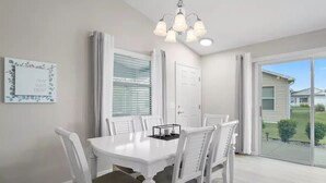 A dining area with a white table and chairs, a chandelier, a door, and a view of the outside.