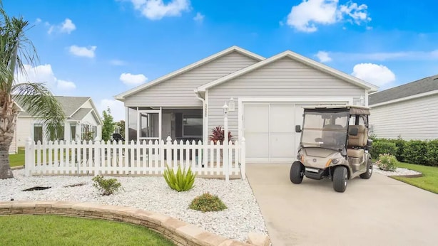 A single-story house with a garage, a white picket fence, and a golf cart parked in the driveway.