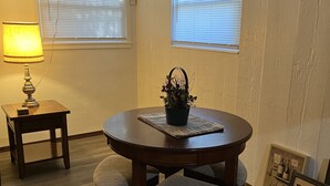 A dining area with a round table, four chairs, a small table with a lamp, and two windows with blinds. - Oasis Studio Downtown Cambridge (Cambridge)