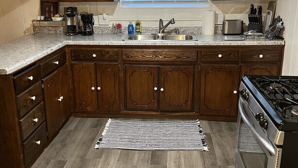 A kitchen with dark wooden cabinets, a stainless steel sink, a gas stove, and a window above the sink. - Oasis Studio Downtown Cambridge (Cambridge)