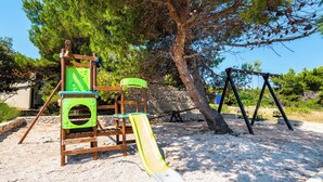 A playground with a slide and swings, surrounded by trees and a stone wall. - Room-caravan Near the sea 1 (Preko)