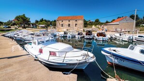 A marina with several boats docked, a stone building with a red roof, and a clear blue sky. - Room-caravan Near the sea 1 (Preko)
