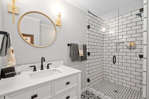 Ein modernes Badezimmer mit einem weißen Waschtisch, einem runden Spiegel und einer Dusche mit weißen Fliesen.